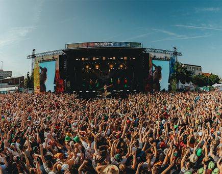 Große Menschenmenge vor einer Bühne mit Beleuchtung und Banner '#oleparty' bei einem Open-Air-Festival