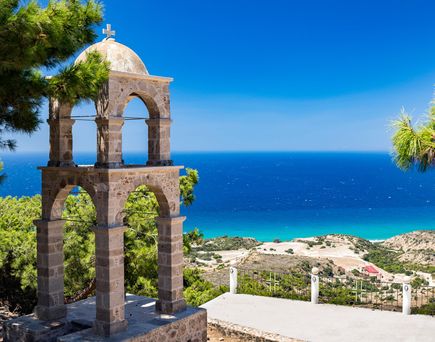 Steinerner Glockenturm mit Kreuz auf einer Anhöhe, Blick auf das blaue Meer und Küstenlandschaft bei Kos