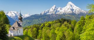 Wallfahrtskirche Maria Gern bei Berchtesgaden in Deutschland vor grünen Wäldern und schneebedeckten Gipfeln der Alpen