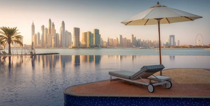 Infinity-Pool mit Liegestuhl und Sonnenschirm, Blick auf die Skyline von Dubai bei Sonnenuntergang vom Dukes The Palm Dubai