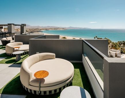 Terrasse mit runden Loungemöbeln und kleinen Tischen, Blick auf Meer und Küste, Teil des R2 Higos Beach Aparthotels.