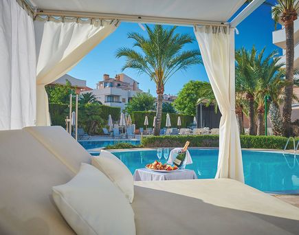 Poolbereich des Hotels Girasol auf Mallorca mit Liege, Tisch, Sektflasche, Gläsern und Palmen im Hintergrund.