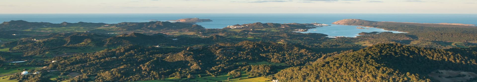 Weitblick vom Monte Toro auf Menorca mit grünen Hügeln, verstreuten Häusern und dem Meer im Hintergrund