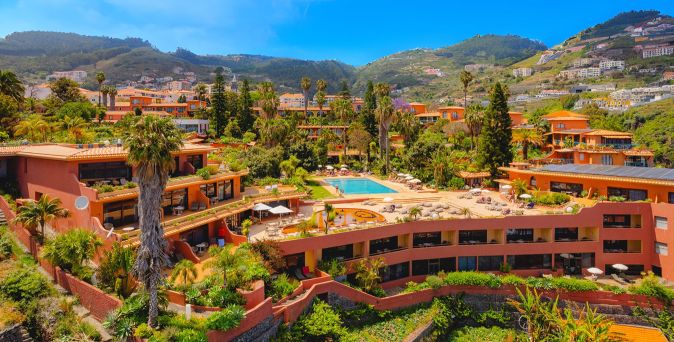 Weitläufige Resortanlage des Quinta Splendida Wellness & Botanical Garden in mediterraner Berglandschaft mit terrakottafarbenen Gebäuden, üppiger Vegetation, Palmen und großem zentralen Poolbereich unter blauem Himmel