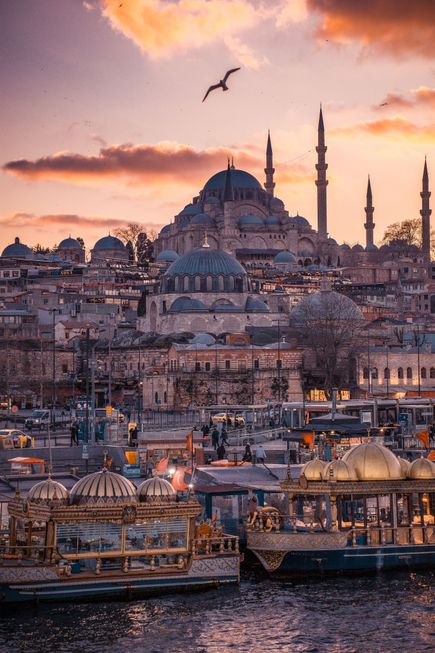 Blick auf die Skyline von Istanbul mit der großen Moschee und mehreren Minaretten im Hintergrund sowie historischen Booten am Wasser im Vordergrund bei Sonnenuntergang.
