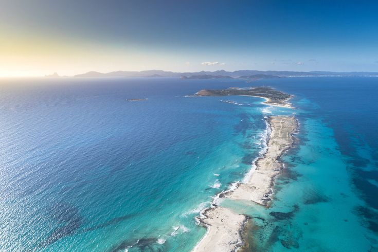 Luftaufnahme der schmalen Sandbank Ses Illetes auf Formentera, umgeben von türkisblauem Meer und mit Blick auf die Nachbarinseln