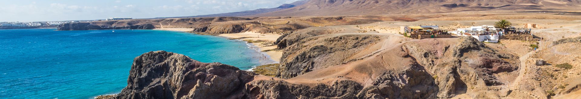 Küstenlandschaft mit felsigen Klippen, blauem Meer und trockenem, hügeligem Hinterland