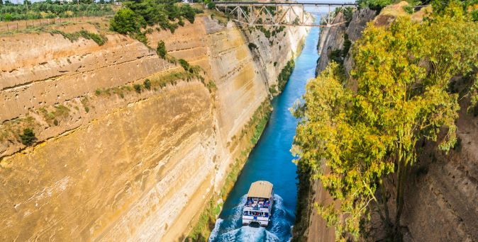 Steinerner Innenhof mit Bänken, Töpfen und blühendem Baum vor mehreren Gebäuden mit roten Ziegeldächern und Rundtürmen unter blauem Himmel.