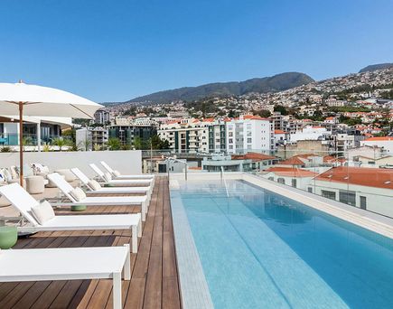 Dachterrasse mit Pool, Liegestühlen und Sonnenschirm vor Stadt- und Bergkulisse