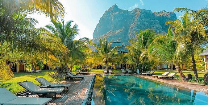Pool mit Liegestühlen und Palmen im Dinarobin Beachcomber Golf Resort & Spa vor Bergkulisse auf Mauritius.