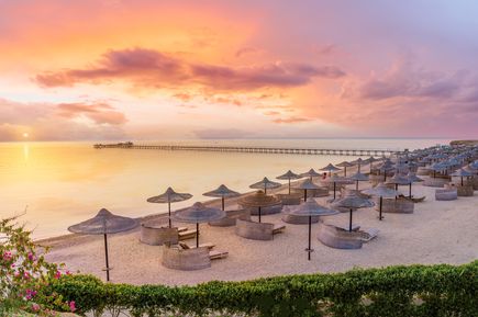 Strand mit Liegen und Sonnenschirmen bei Sonnenuntergang, langer Steg im ruhigen Meer in Marsa Alam