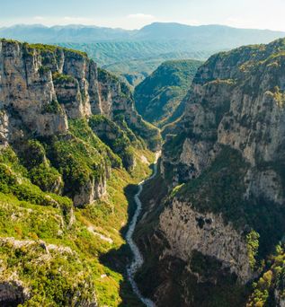 Tiefe Schlucht mit steilen, bewaldeten Felswänden und einem schmalen Flusslauf in der Vikos-Schlucht, Griechenland.