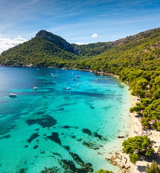 Strand Playa de Formentor auf Mallorca mit kristallklarem Wasser, dichtem Pinienwald und Segelbooten in der Bucht