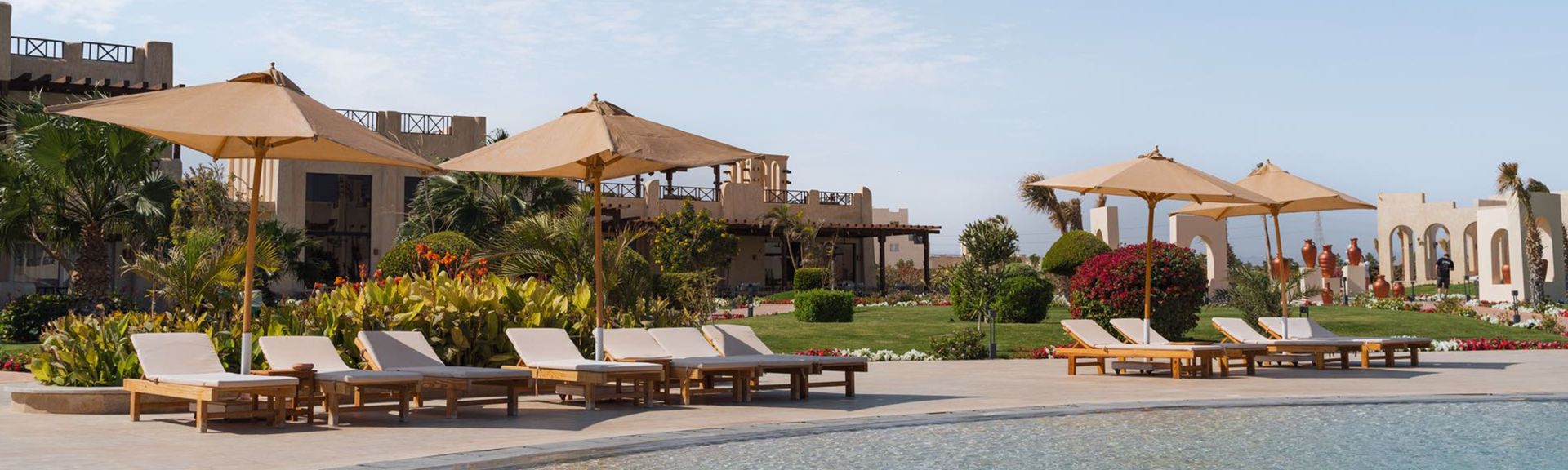 Liegestühle mit Sonnenschirmen am Pool des True Beach Resorts in Ägypten, umgeben von Palmen und Gebäuden im Hintergrund