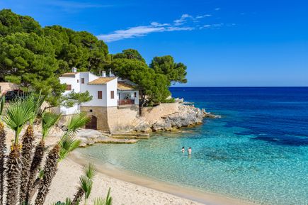 Idyllische Bucht Cala Ratjada auf Mallorca mit weißem Haus am Strand, klarem Wasser und Pinien im Hintergrund