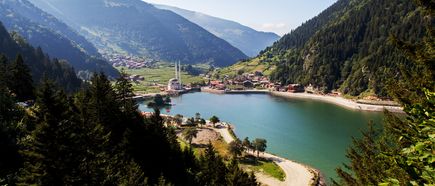 Uzungöl in der Türkei: grüner Bergsee im Tal, umgeben von dichten Wäldern, mit Dorf und Moschee am Ufer
