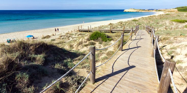 Holzsteg durch Dünen zum Sandstrand von Son Bou auf Menorca mit türkisblauem Meer im Hintergrund