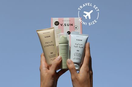 Hände halten das V.SUN Premium Travel Set mit Sonnencreme und Pflegeprodukten in Reisegröße vor blauem Hintergrund. Im Bild ist der Schriftzug „Travel Set Mini Size“ zu sehen.