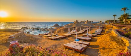 Sonnenuntergang über einem ruhigen Strand mit Liegen und Strohdächern in Marsa Alam am Roten Meer
