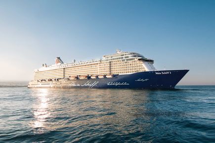 Das Kreuzfahrtschiff Mein Schiff 3 fährt bei sonnigem Wetter über das Meer und ist seitlich von vorn abgebildet.