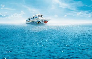 Kreuzfahrtschiff AIDAblu mit blau-gelbem Augendesign sowie rotem Kussmund auf dem Bug fährt auf ruhiger See unter blauem Himmel.