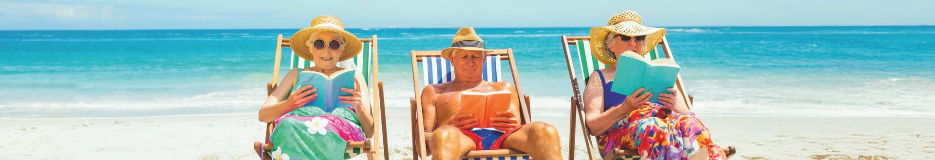 Drei Personen sitzen in Liegestühlen am Strand und lesen Bücher vor dem Hintergrund des blauen Meeres