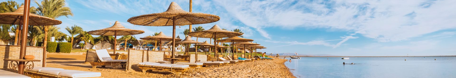 Strand mit Liegestühlen und Sonnenschirmen aus Stroh am Roten Meer unter blauem Himmel