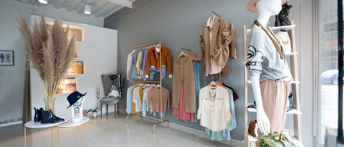 Ladenlokal mit vielen bunten Kleidungsstücken, im Vordergrund ein Mannequin mit rosa Hut.