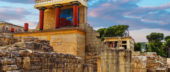 Segelboot auf türkisblauem Wasser vor einem Küstenort mit weißen Häusern auf einem Hügel und Bergen im Hintergrund.