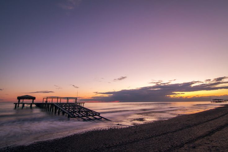 Verlassener Holzsteg am Strand von Belek in der Türkei bei Sonnenuntergang, ruhiges Meer und violett-orangefarbener Himmel