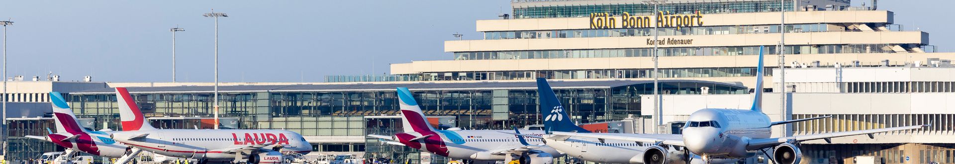 Mehrere Passagierflugzeuge verschiedener Fluggesellschaften vor dem Terminal des Flughafens Köln/Bonn mit sichtbar beschriftetem Hauptgebäude „Köln Bonn Airport Konrad Adenauer“