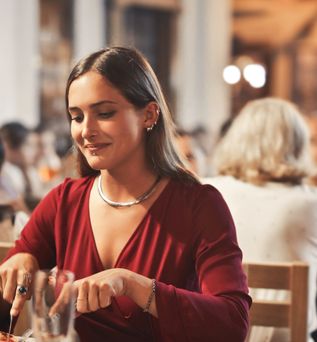 Junge Frau sitzt in einem Restaurant im Freien und genießt ihr Abendessen in gemütlicher Atmosphäre