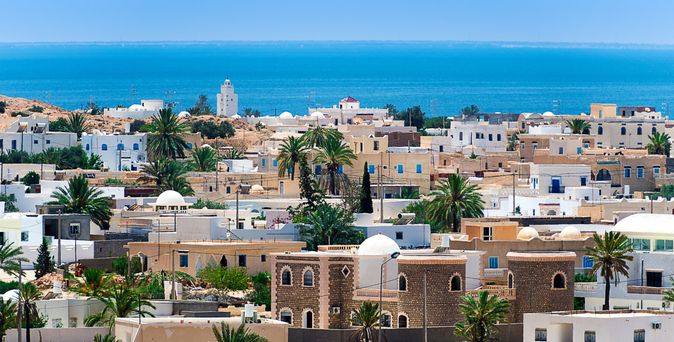 Blick auf ein Dorf mit weißen und beigen Häusern, Palmen und dem Meer im Hintergrund
