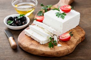 Block Feta-Käse auf Holzbrett, in Scheiben geschnitten, mit Oliven, Tomaten, Petersilie und Olivenöl