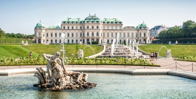 Barockschloss Belvedere mit grünen Kuppeln, davor Springbrunnen mit Skulpturengruppe in einem Wasserbecken, umgeben von Rasen und Wegen