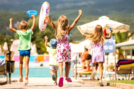 Vier Kinder laufen fröhlich mit Schwimmreifen zu einem Hotelpool in einer Ferienanlage