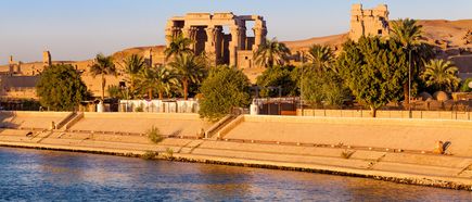 Kom-Ombo-Tempel mit Säulen und Ruinen hinter Palmen am Ufer des Nils bei Sonnenlicht