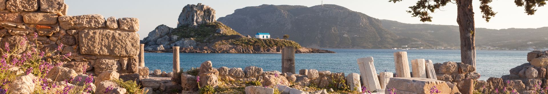 Ruinen einer antiken Säulenhalle mit Blick auf das Meer und eine felsige Insel im Hintergrund