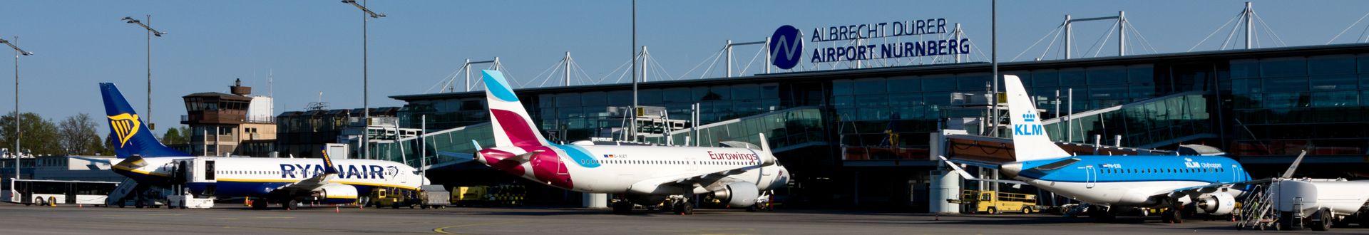Mehrere Passagierflugzeuge von Ryanair, Eurowings und KLM stehen auf dem Vorfeld des Albrecht Dürer Airport Nürnberg vor dem Terminalgebäude mit sichtbar ausgeschildertem Flughafennamen.