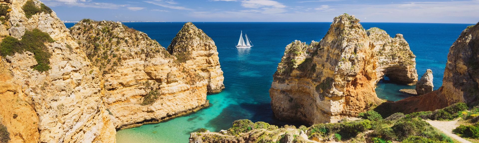 Felsige Küstenformationen mit türkisfarbenem Wasser und einem Segelboot im Meer an der Algarve in Portugal