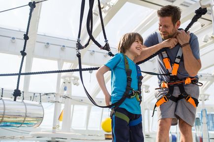 Vater und Sohn mit Klettergurten stehen in einem Klettergarten auf einem Schiff