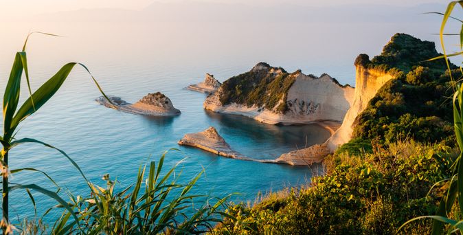 Blick auf die felsige Küste und das blaue Meer der Insel Korfu in Griechenland, mit grüner Vegetation im Vordergrund