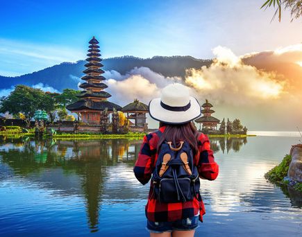 Frau mit Rucksack und Hut blickt auf den Pura Ulun Danu Bratan Tempel am See in Bali bei Sonnenaufgang