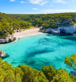 Idyllische Bucht Cala Mitjaneta auf Menorca mit weißem Sandstrand, türkisfarbenem Wasser und von Klippen umgeben
