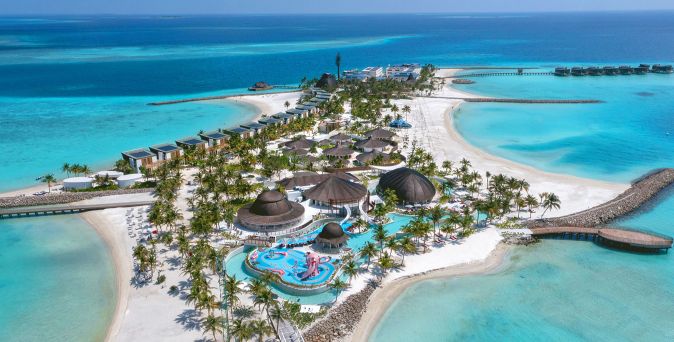 Luftaufnahme des Centara Mirage Lagoon Maldives mit weißem Sandstrand, türkisfarbener Lagune, Palmen und mehreren Poolbereichen