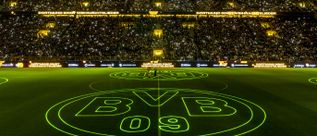 Fußballstadion bei Nacht mit leuchtendem BVB-09-Logo und Text 'Dortmund singt Weihnachtslieder' auf der Tribüne