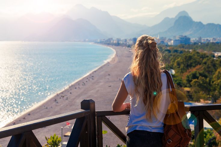 Person steht auf einer Terrasse mit weitem Blick über die Küste von Antalya in der Türkei, türkisblaues Meer und grüne Landschaft im Hintergrund