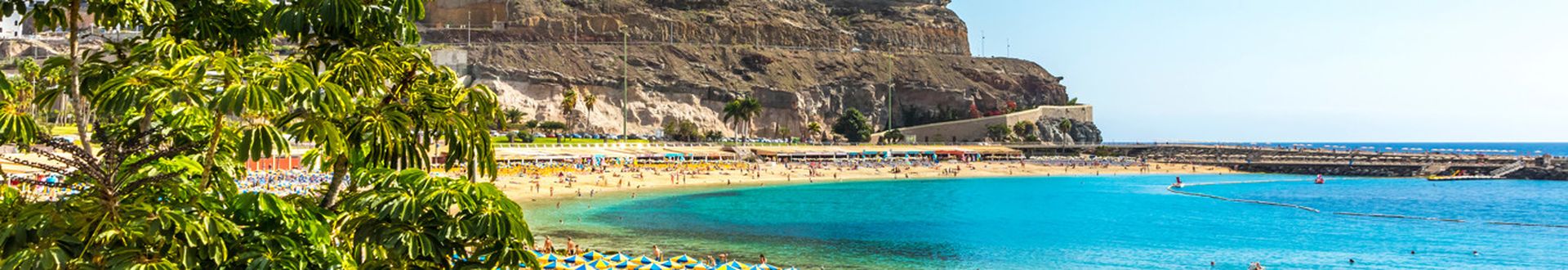 Blick auf den Playa de Amadores auf Gran Canaria mit türkisblauer Badebucht, gelben Sonnenschirmen, Sandstrand und Hotels auf den Klippen oberhalb der Küste