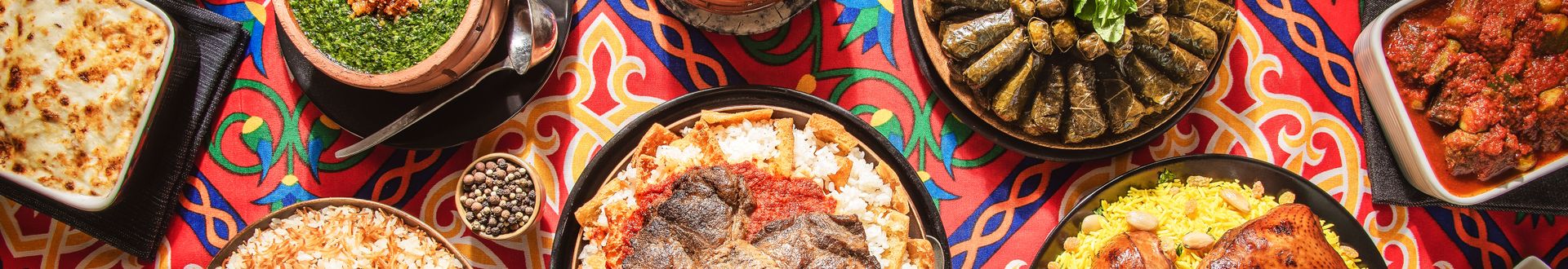Verschiedene orientalische Gerichte wie gefüllte Weinblätter, gebackenes Fleisch, Reis und Gemüse werden auf einem bunten Tuch serviert