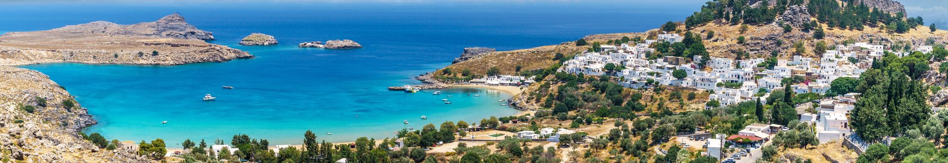 Luftaufnahme der Küste von Lindos auf Rhodos mit weiß getünchten Häusern, einem Hafen und klarem blauem Meer.